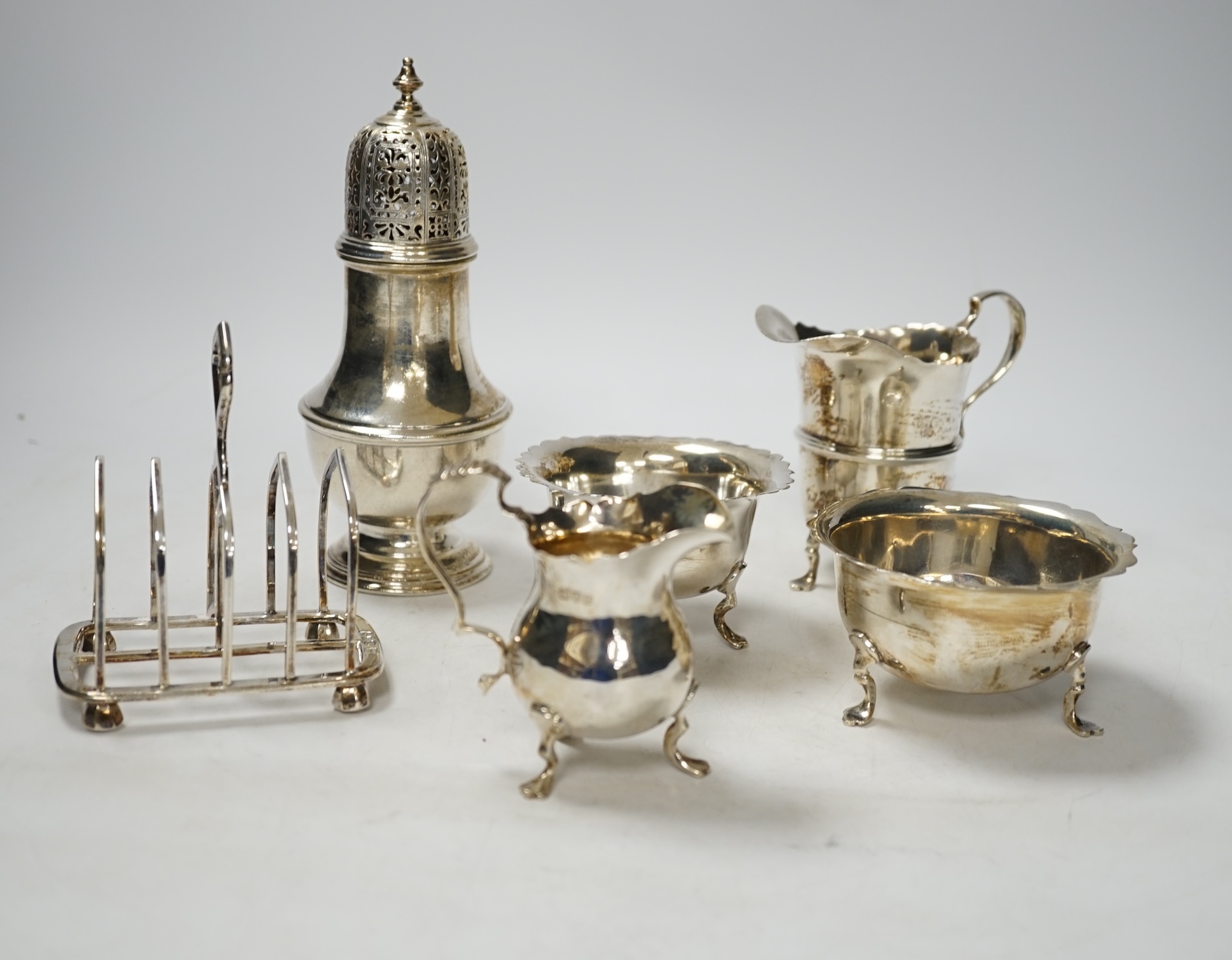 Two 20th century silver cream jugs, two silver sugar bowls, a silver toastrack and a silver caster, 18.5oz.